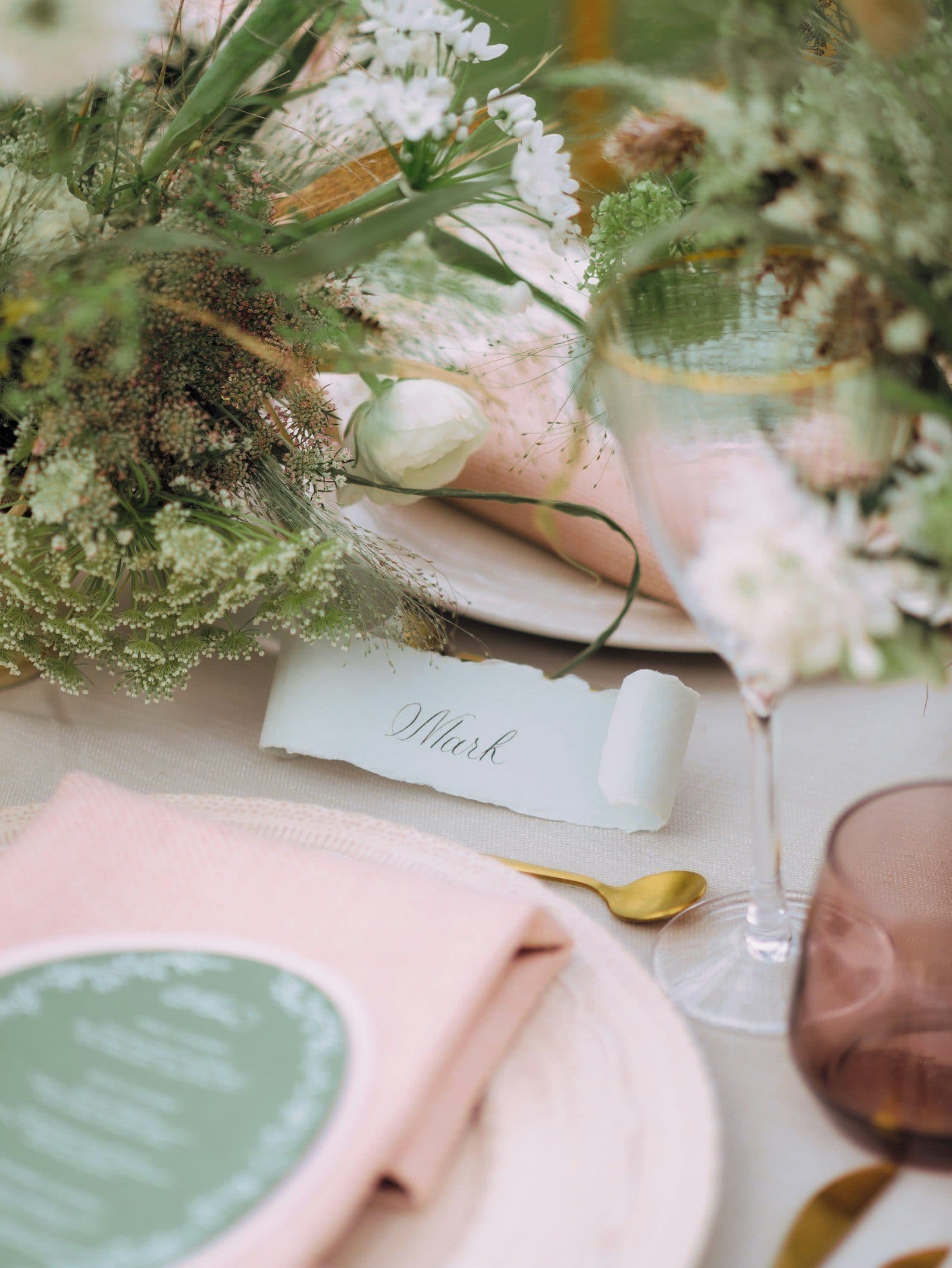 A hand-lettered place card on a set wedding table